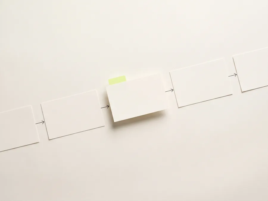 A row of blank cards joined by inked arrows, one card lifted mid-handover with a lime tab clipped to it.
